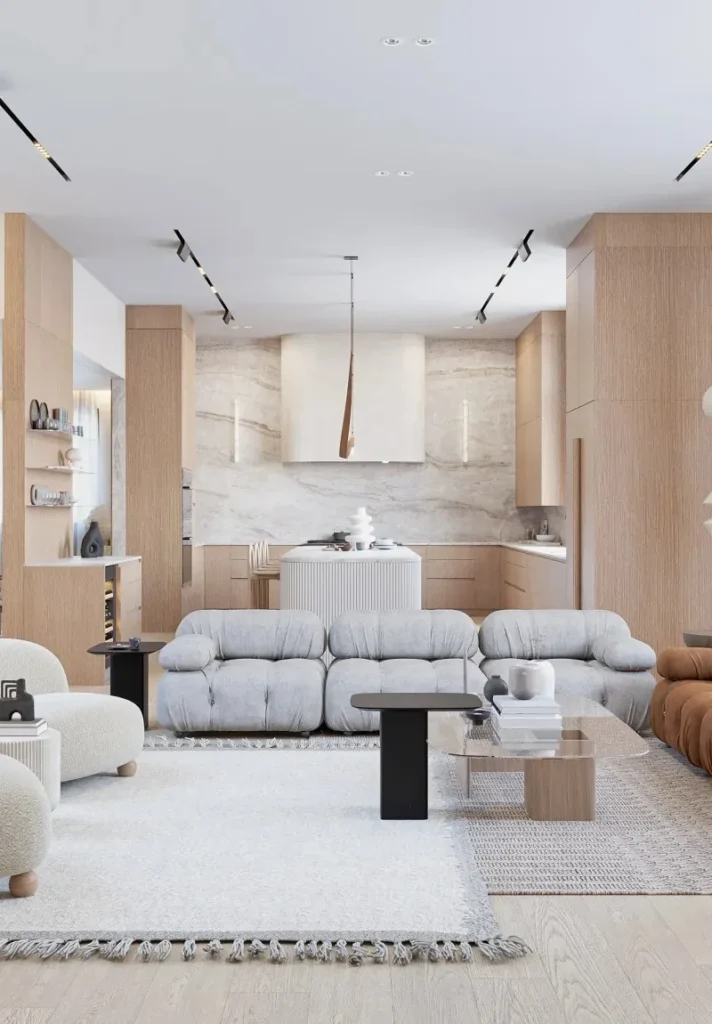 Modern open-plan living room with light wood, grey sofas, and kitchen area.